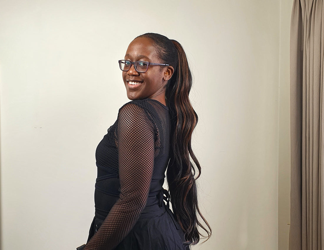 A young woman stands looking backwards at the camera. Her hair is slicked back and tied into a ponytail extension, the LuluPony Viki in black with brown streaks through it.